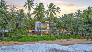 Ein Strandhotel mit mehreren Etagen, Palmen und einem Sandstrand.
