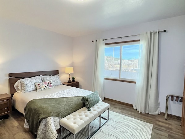 A bedroom with a bed, bedside tables, a bench, a window with curtains, and a view outside.