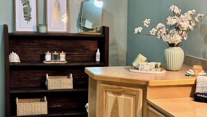 Une salle de bain avec un meuble-lavabo en bois, une étagère ornée d’illustrations botaniques encadrées, un miroir et un vase rempli de fleurs.