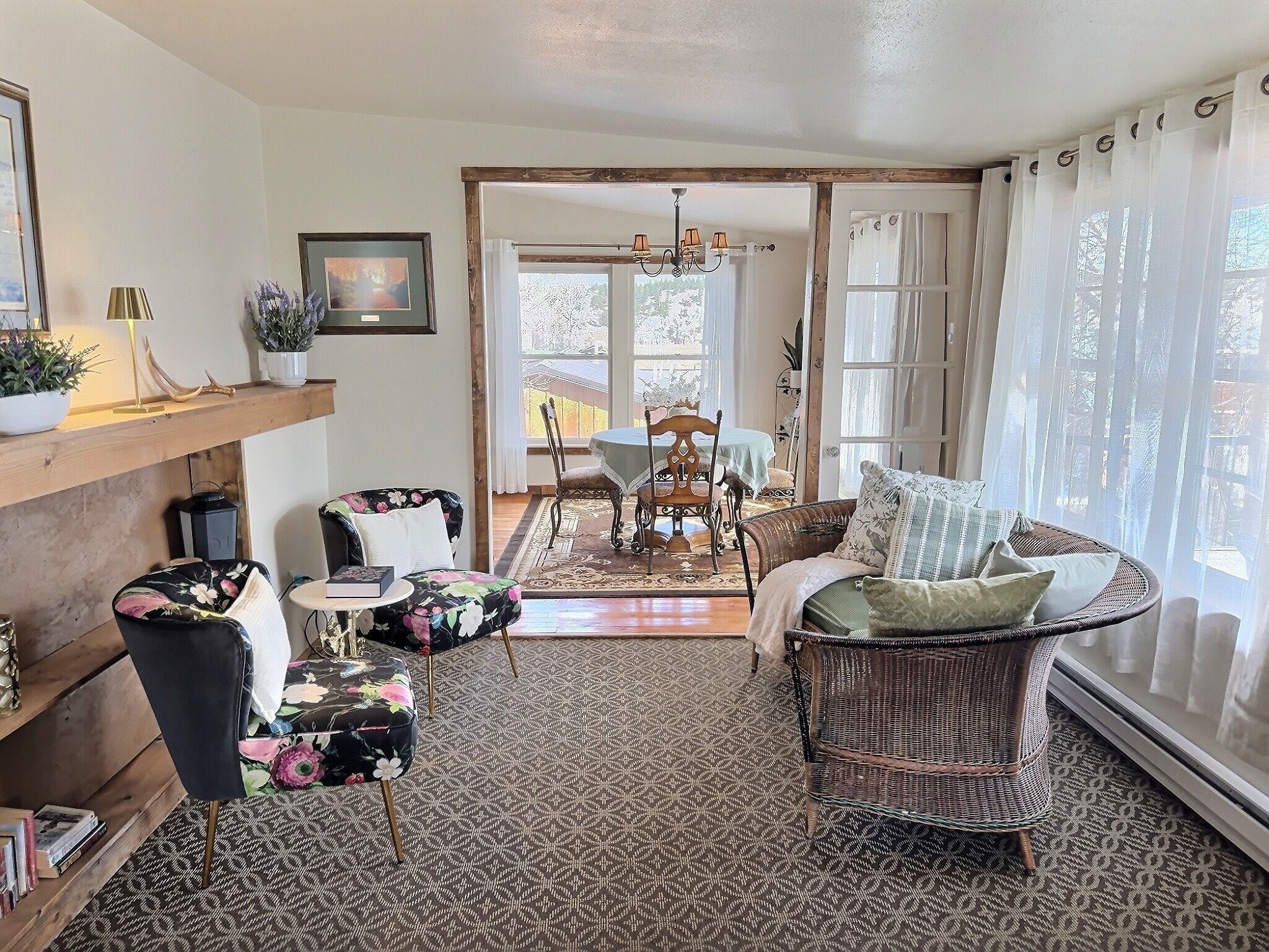 A cozy living room with a fireplace, a dining area, and a large window with sheer curtains.