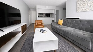 En moderne stue med et fladskærms-tv, en grå sofa, et hvidt sofabord og en læderstol i brunt.
