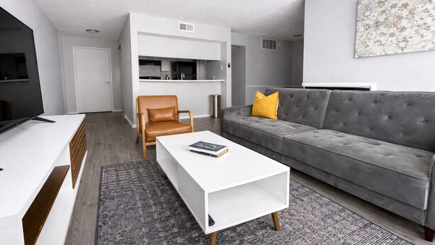 En moderne stue med sofa, lænestol, sofabord og et køkken i baggrunden.