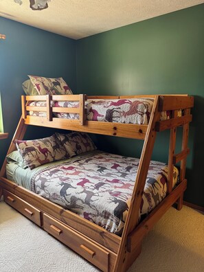 Una cama litera con colcha estampada, estructura de madera y un cajón debajo de la cama inferior.