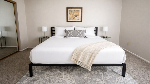 Ein Schlafzimmer mit einem Bett, zwei Nachttischen, einem Spiegel und einem gerahmten Bild an der Wand.