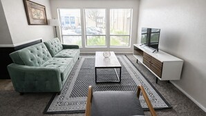 Ein Wohnzimmer mit einem grünen Sofa, einem Couchtisch, einem Fernseher und einem gemusterten Teppich.