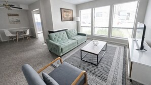 Ein modernes Wohnzimmer mit einem grünen Sofa, einem Couchtisch, einem Fernseher und einem Essbereich mit Stühlen.