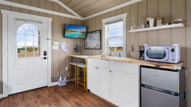 Une cuisine avec des meubles en bois, un four à micro-ondes, un réfrigérateur, un tabouret en bois, une télévision et une fenêtre donnant sur un beau paysage.