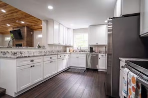 A modern kitchen with white cabinets, a wooden ceiling, and a stainless steel refrigerator. - Wooded Retreat + 1.3 Acres/Fire Pit/King Bed/Hiking/Near Sewanee & Caverns (Monteagle)