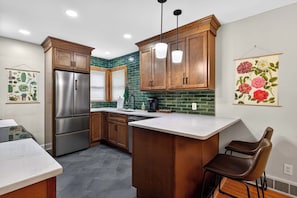 A kitchen with wooden cabinets, a stainless steel refrigerator, a bar island, and hanging floral artwork.