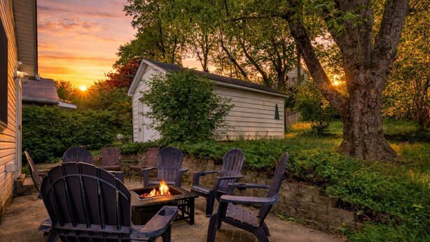 Un patio con sillas Adirondack, un brasero y un cobertizo pequeño en un jardín.