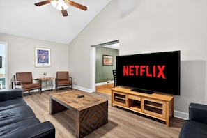 A living room with a large TV displaying 'NETFLIX,' a ceiling fan, a wooden coffee table, and two leather sofas.