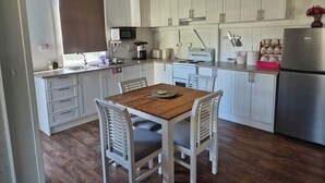 A compact kitchen with white cabinets, a wooden dining table, and a stainless steel refrigerator. - Linville Cottage. This is a 100 year old cottage in town close to rail trail. (Linville)