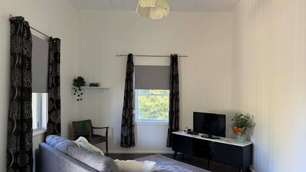 A room with a grey sofa, a desk with a TV, a hanging plant, and a window with curtains. - Linville Cottage. This is a 100 year old cottage in town close to rail trail. (Linville)