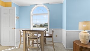 A room with a dining table and chairs, a window with a view, a lamp, and a door. - "Dibbs on Holden" 3 Bedroom, 3 Bathroom, Canal Home (Holden Beach)