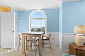 A room with a dining table and chairs, a window with a view, a lamp, and a door. - "Dibbs on Holden" 3 Bedroom, 3 Bathroom, Canal Home (Holden Beach)