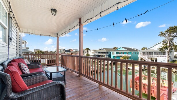 A covered porch with wicker furniture and a view of a water body and buildings. - "Dibbs on Holden" 3 Bedroom, 3 Bathroom, Canal Home (Holden Beach)