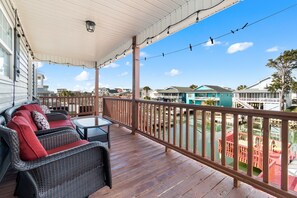 A covered porch with wicker furniture and a view of a water body and buildings. - "Dibbs on Holden" 3 Bedroom, 3 Bathroom, Canal Home (Holden Beach)
