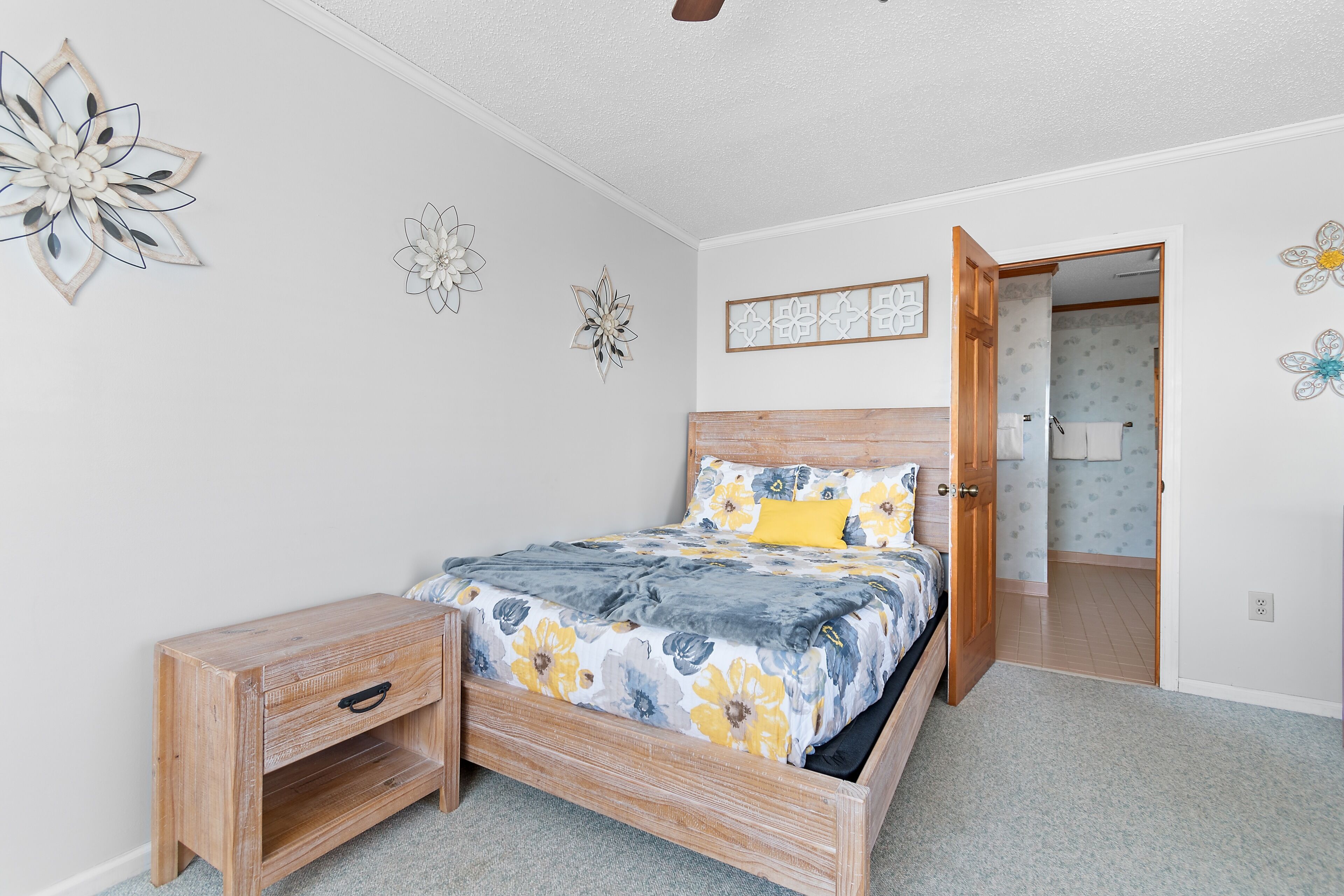 A bedroom with a wooden bed, a nightstand, a door leading to another room, and wall decorations.