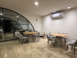 A modern conference room with round tables, grey chairs, a glass wall, and an air conditioning unit. - Iks' Túun Mérida Department (Conkal)