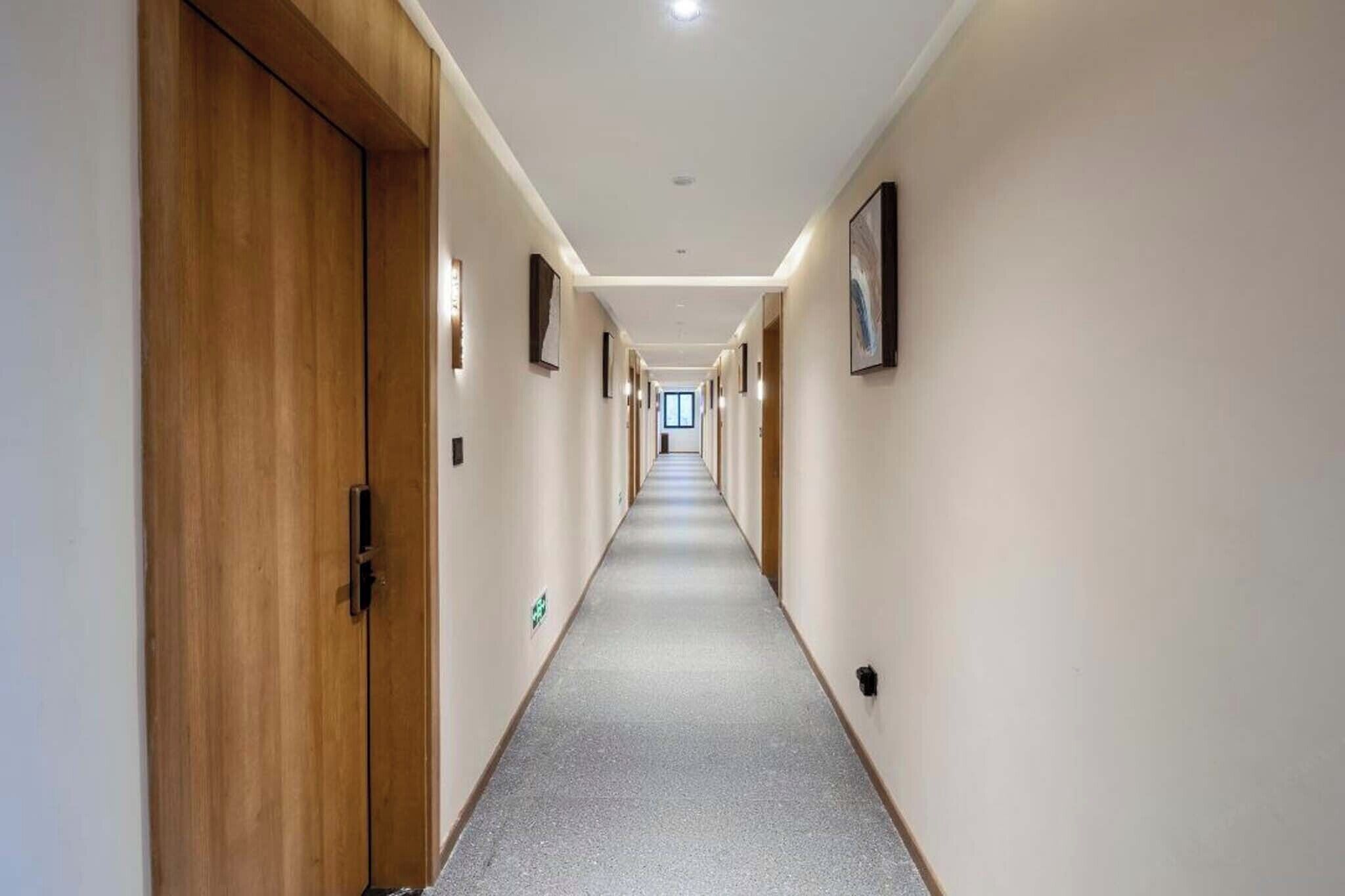 Ein langer, schmaler Hotelkorridor mit Holztüren an einer Seite und gerahmten Bildern an der anderen.