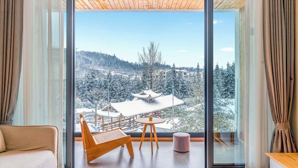 A modern room with a large window, a wooden ceiling, a sofa, a small table, and a chair. - Qixiannv Homestay Xiannv Mountain Shop (Chongqing)