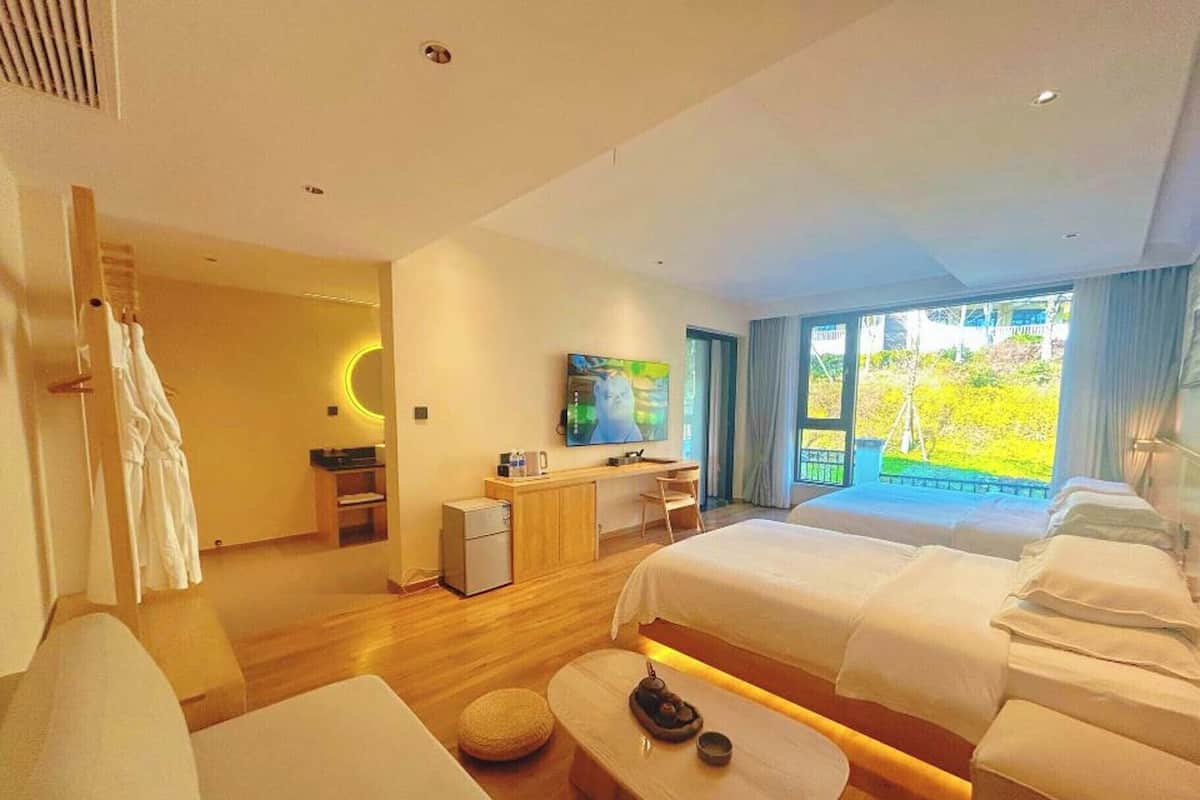 A hotel room with two beds, a desk, a TV, and a balcony with a view.