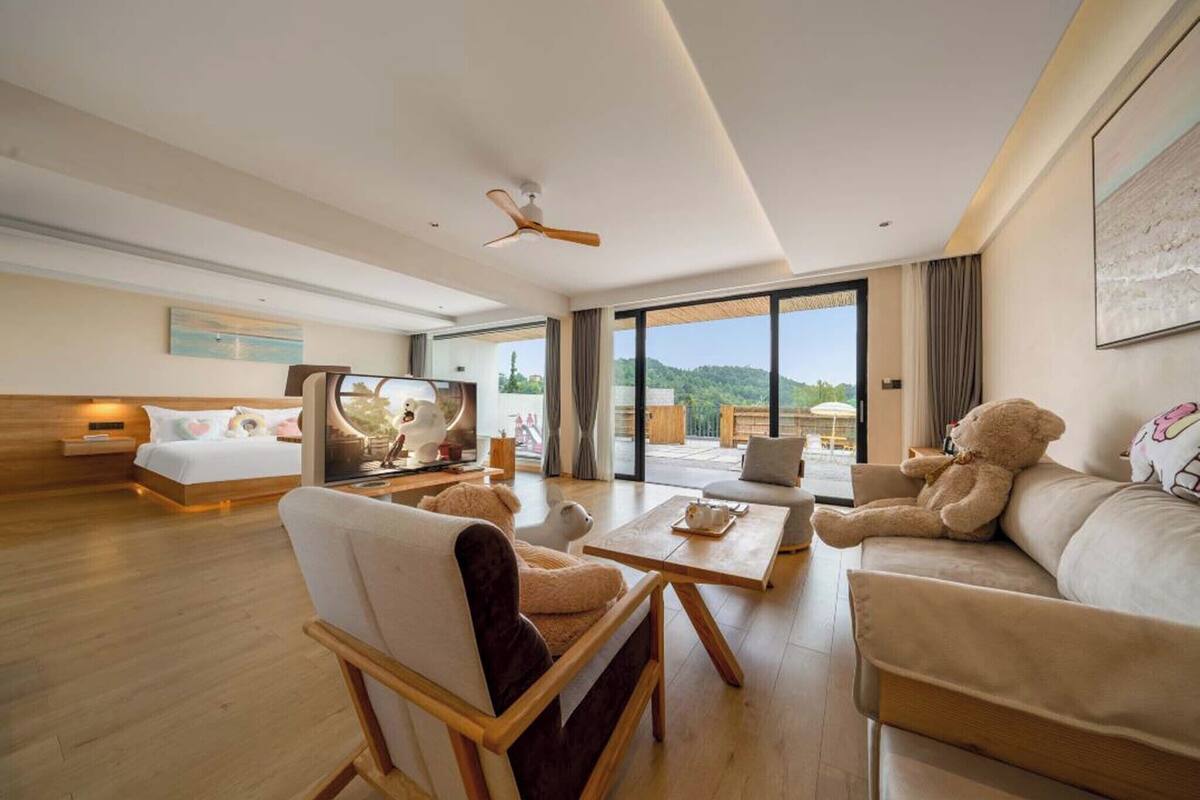 A spacious hotel room with a bed, a sofa, a chair, a coffee table, and a large window offering a view of the outdoors.