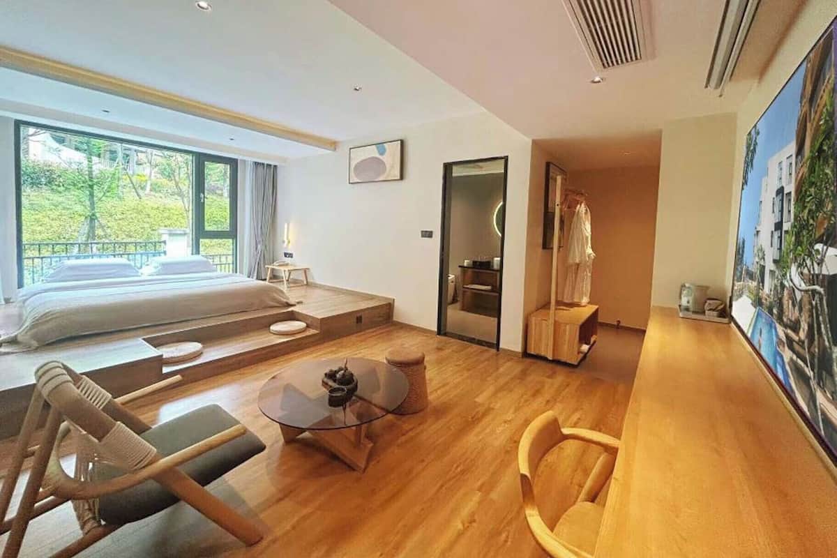 A modern hotel room with a bed, seating area, and a view of greenery.