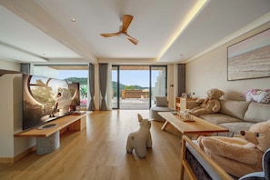 Una sala de estar moderna con un televisor de pantalla plana grande, un ventilador de techo y un sofá con un oso de peluche.