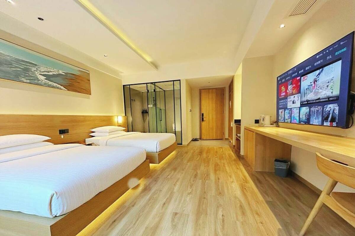 A hotel room with two beds, a TV, and a wooden floor.