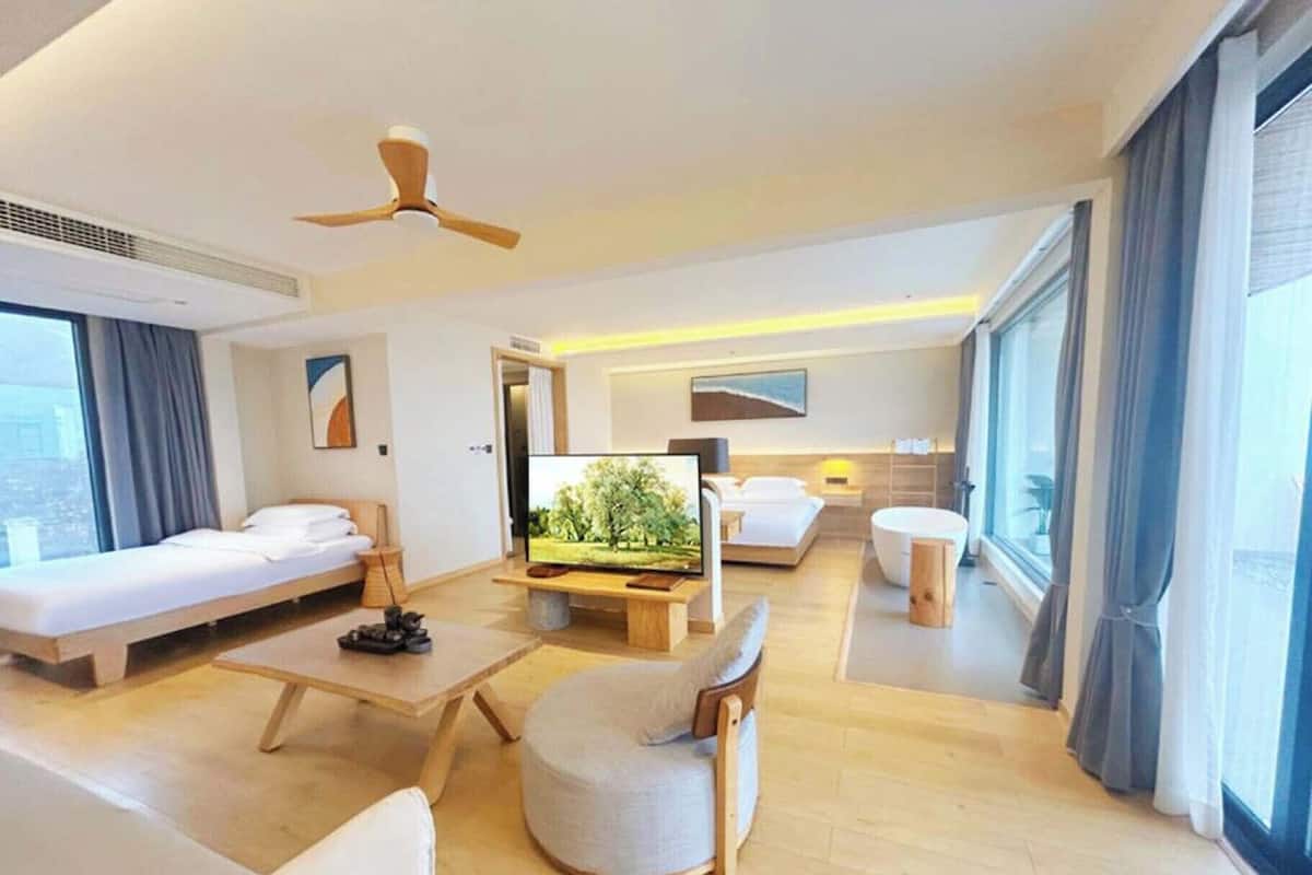 A modern hotel room with a bed, a TV, a desk, a chair, and a large window.
