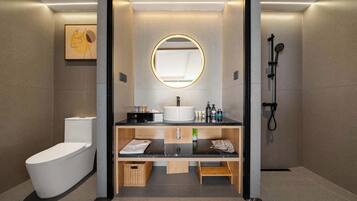 A modern bathroom with a toilet, sink, mirror, shower, and a small wooden shelf.
