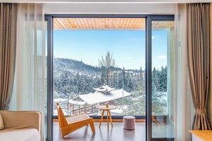 Quarto moderno com uma janela grande, teto de madeira e vista para uma paisagem nevada.