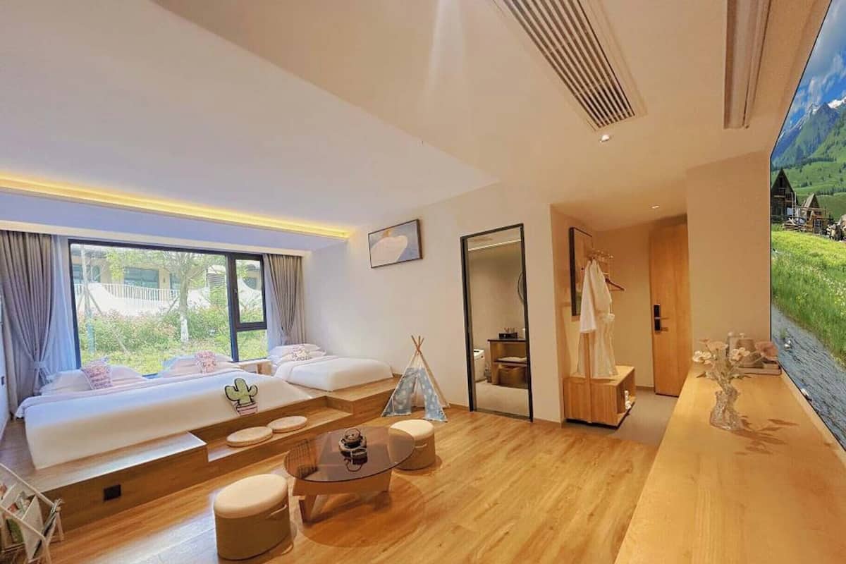 A modern hotel room with a large bed, a sofa, a small table, and a view of a mountain landscape.