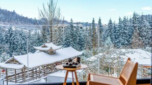 A room with a view of snow-covered trees and buildings, a wooden bench, and a small table with a decorative item. - Qixiannv Homestay Xiannv Mountain Shop (Chongqing)