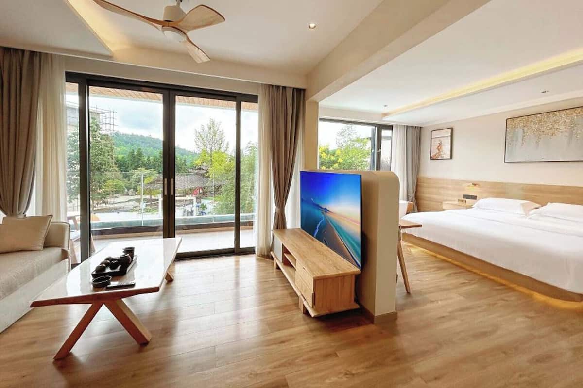 A hotel room with a bed, a TV, a desk, and a balcony with a view.