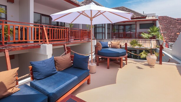 A balcony with a white umbrella, wooden furniture, and potted plants. - Casa Kai (Gili Trawangan)