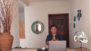 A person sitting at a desk with a laptop, a potted plant, and decorative wall art. - Casa Kai (Gili Trawangan)