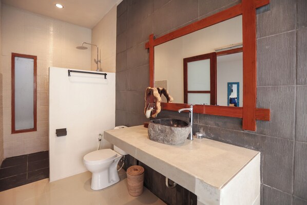 A bathroom with a white toilet, a stone sink, and a large mirror with a wooden frame. - Casa Kai (Gili Trawangan)