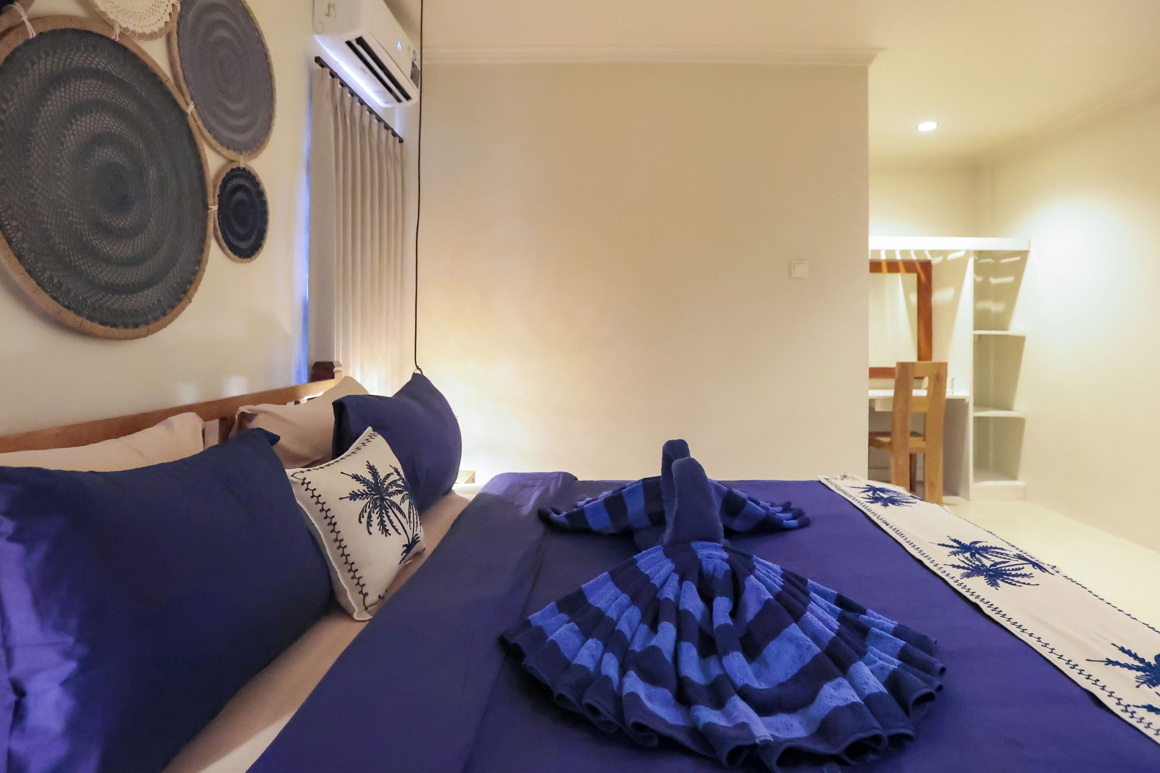 A bed with blue bedding, a pillow with a palm tree design, and a striped towel.
