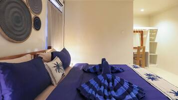 A bed with blue bedding, a pillow with a palm tree design, and a striped towel.