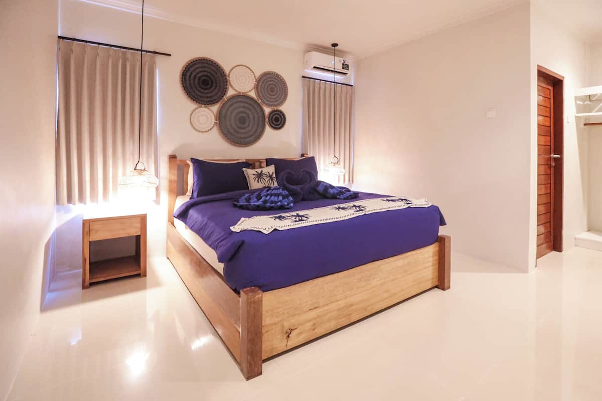 Un dormitorio con una cama de madera, una mesita de noche, aire acondicionado instalado en la pared y una puerta.