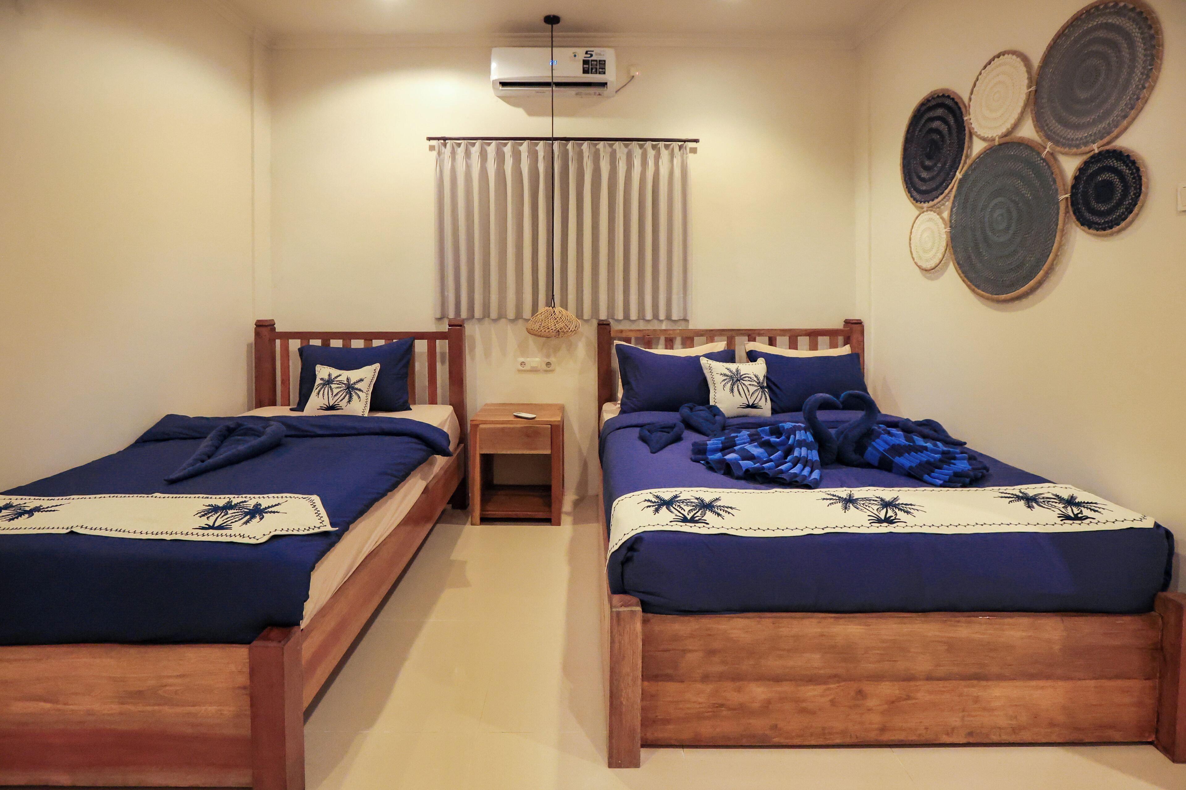 Una habitación con dos camas de madera, una mesita de noche pequeña, aire acondicionado instalado en la pared y una cortina.