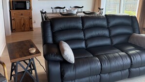 Uma sala de estar moderna com um sofá de couro preto, mesa de jantar de madeira e uma cozinha com micro-ondas.