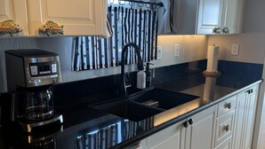 Cozinha moderna com armários brancos, bancada preta, cafeteira e máquina de lavar louça.