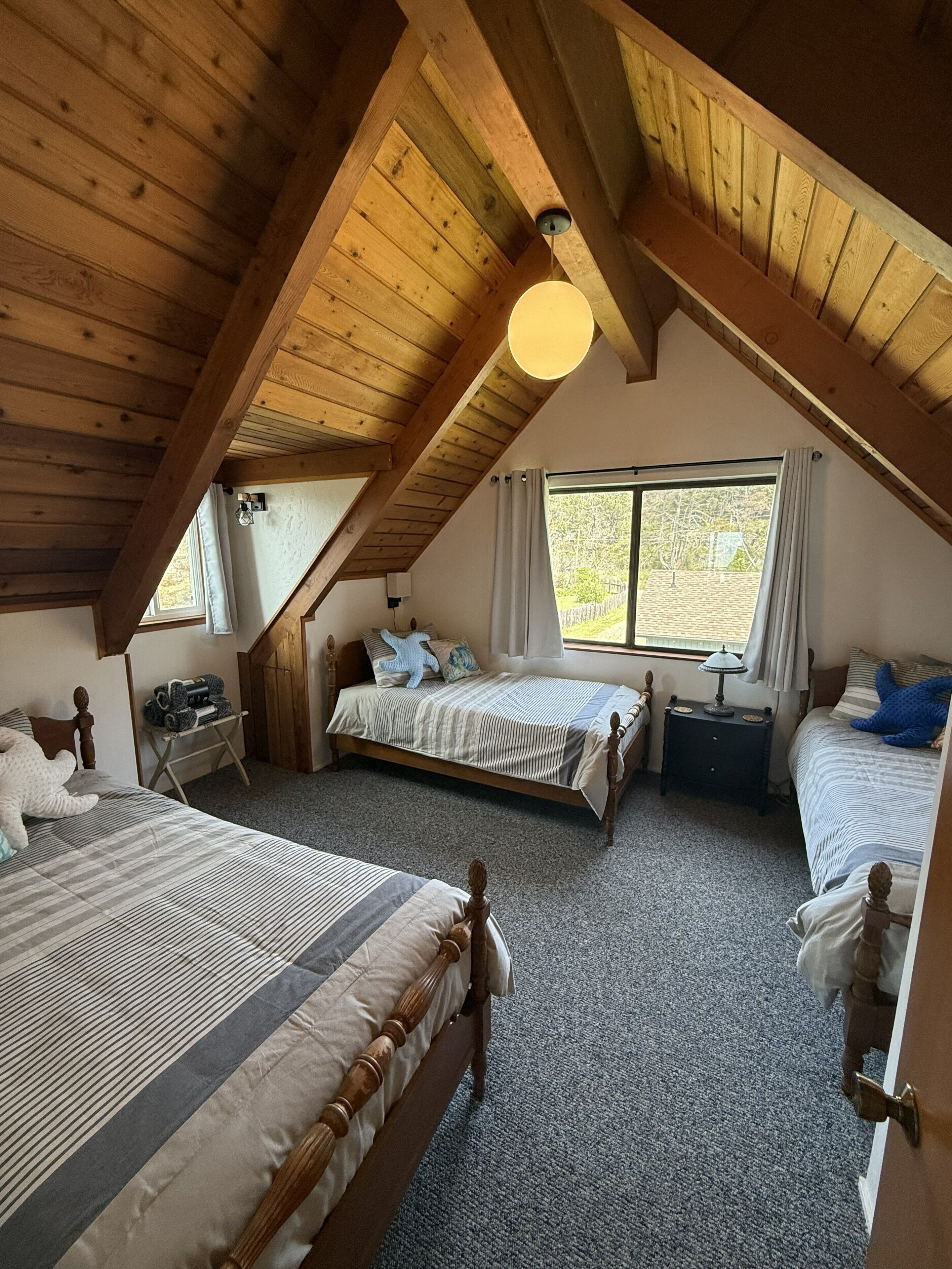 A cozy attic bedroom with two beds, a wooden ceiling, and a window with curtains.