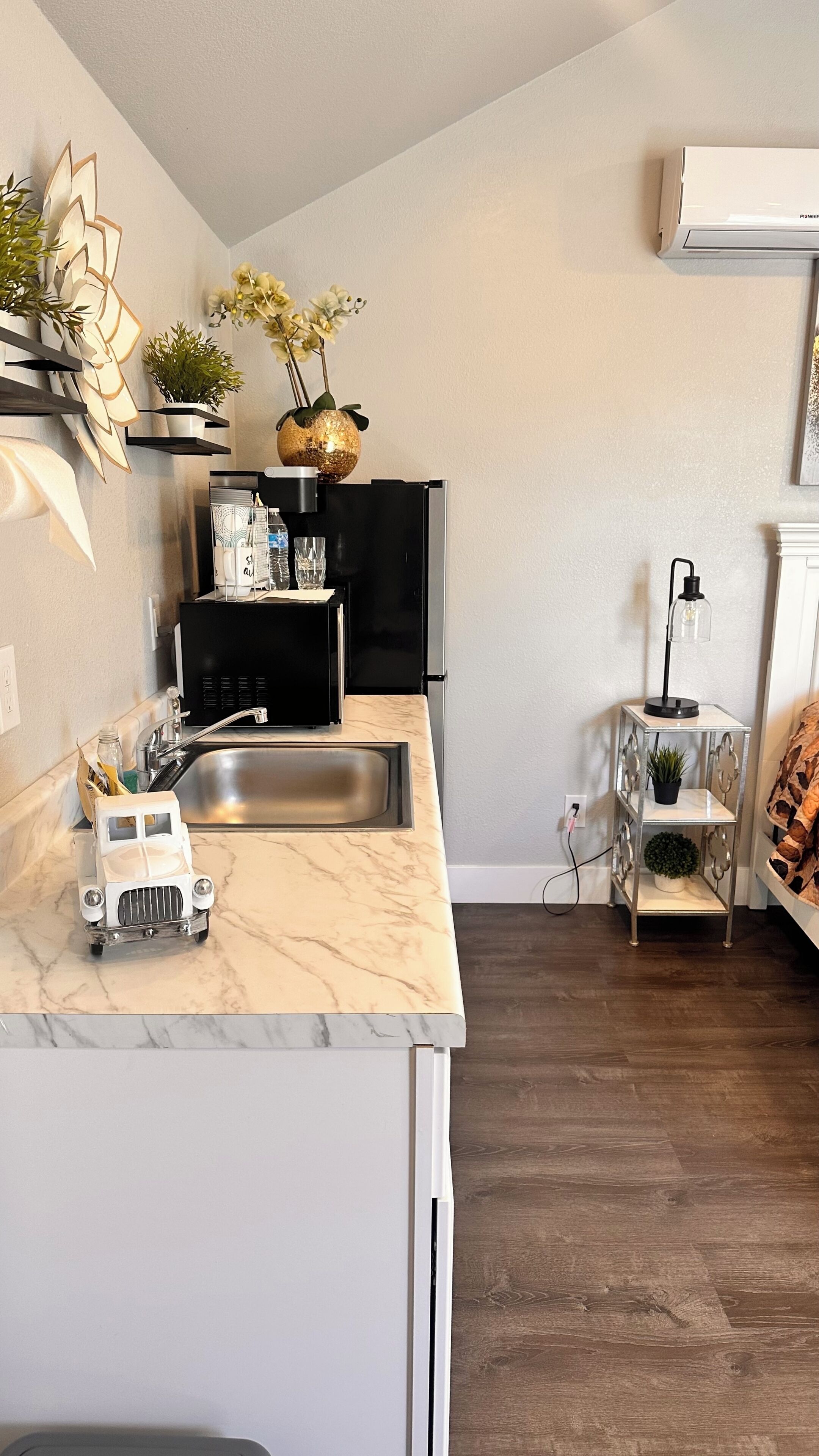 A compact kitchen with a sink, black appliances, a marble countertop, and a small side table with a plant.