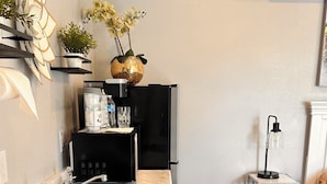 Cocina compacta con lavamanos, electrodomésticos negros, encimera de mármol y una pequeña mesita con una planta.