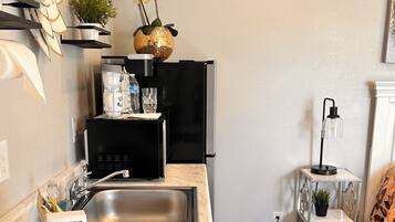 A compact kitchen with a sink, black appliances, a marble countertop, and a small side table with a plant.