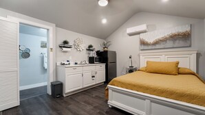 Un dormitorio con cama, muebles blancos, una pequeña cocina y un adorno en la pared.